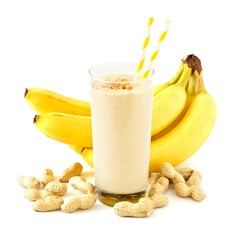 Peanut butter banana smoothie in a glass with straws and scattered peanuts and bananas over white