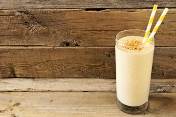 Peanut butter banana oat breakfast smoothie with paper straws against a rustic wood background