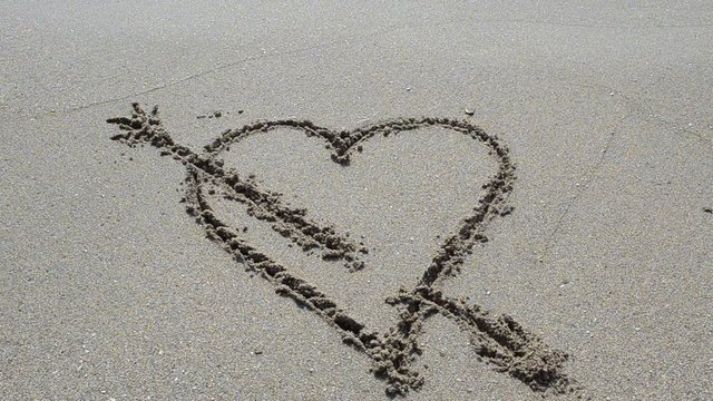 Wave washes over heart in the sand. Love and heart break concept.