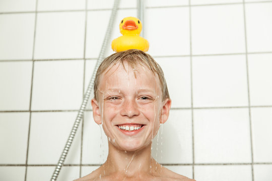 Smiling boy showering with rubber ducky on head