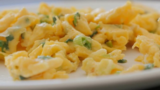 Beaten eggs and scallion breakfast on plate close-up pan 4K 2160p 30fps UHD video - Panning on plate with eggs scrambled fried as omelette 4K 3840X2160 UltraHD footage 