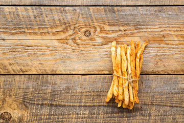 Heap of homemade bread sticks on wooden table with straw