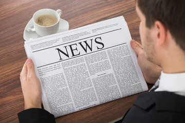 Businessman Reading Newspaper At Desk