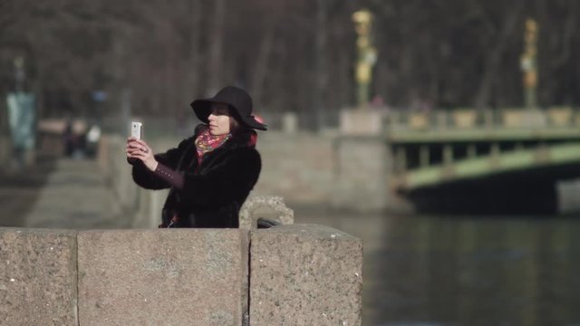 A pretty women in black hat makes selphy on the bridge in  european city.