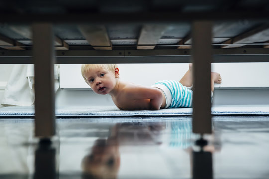 Baby boy peering under bed