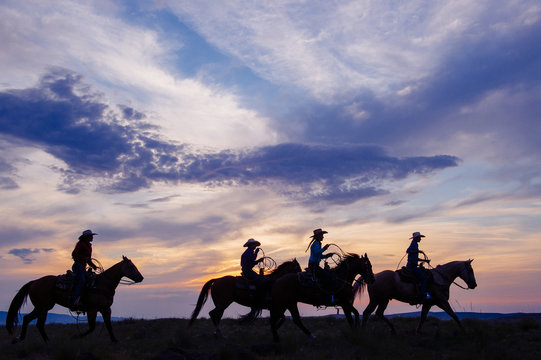 Cowgirls and cowboy riding horses at sunset
