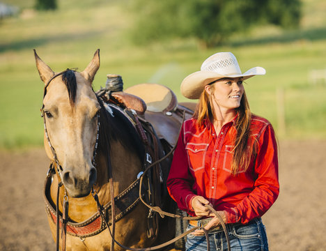 Caucasian cowgirl walking horse on ranch
