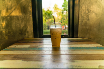 capuchino Ice coffee in plastic cup with straw on wooden table and window at day light - copy space
