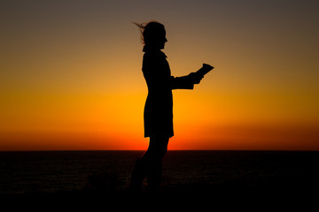 Teen girl reading book outdoors at sunset time