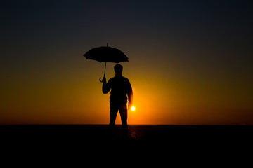 Man holding and umbrella in silhouette against  orange sunset