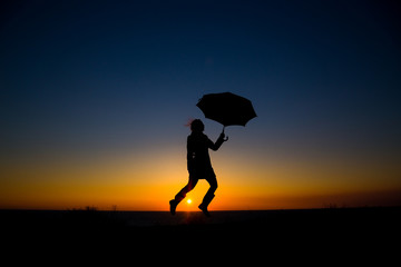 Woman holding and umbrella in silhouette against  orange sunset