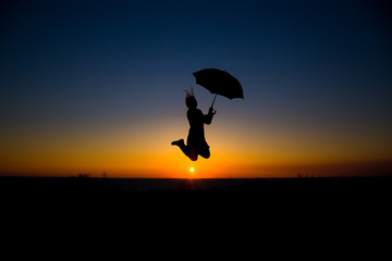 Woman holding and umbrella in silhouette against  orange sunset