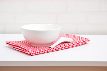 Empty white bowl and spoon on red tablecloth over table with brick wallpaper background