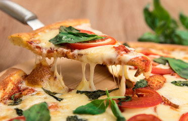 Pizza Margherita with tomatoes, mozzarella and basil on a wooden background, a slice of pizza with cheese stretching, close-up