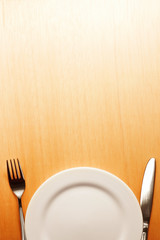 Photo of the fork and knife with white plate on wood