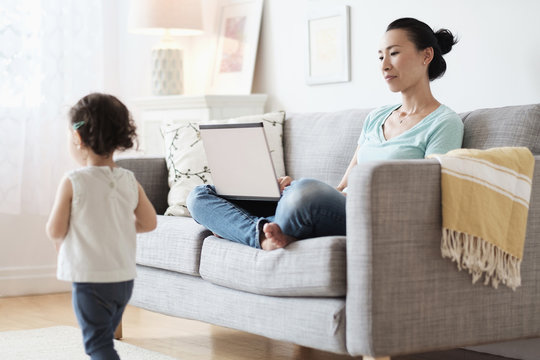Mother using laptop, ignoring baby daughter