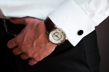 cufflinks. male style male with cuff links on his shirt and a clock. a man holds his belt. close-up