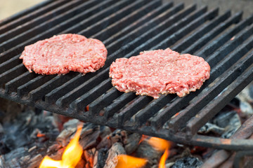 Two raw hamburger slices cooking on grill with flames