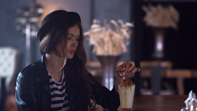 Young attractive Caucasian girl with a milk shake in modern cafe. 4K cinemagraph - motion photo seamless loop