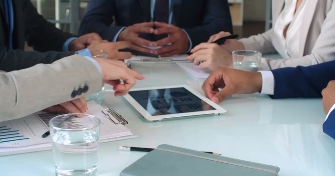 Close up of businessmen hands using tablet to work with financial diagrams on the meeting