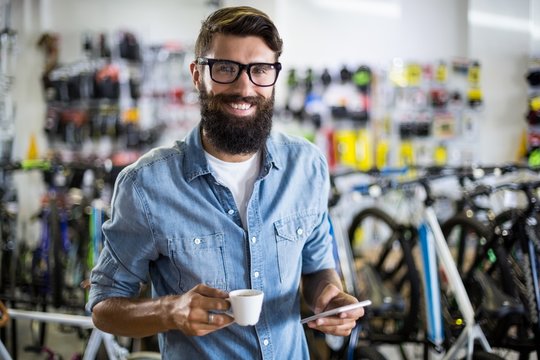 Bike mechanic checking at smartphone and having coffee