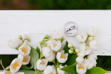 Golden wedding rings with diamonds lie inside jasmine (Philadelphus) flower in bridal bouquet. Wedding bouquet. Bride's traditional symbolic accessory. Floral composition with jasmine flowers.