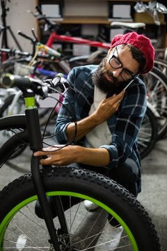 Bike mechanic checking at bicycle and being on the phone