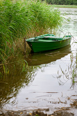 Naklejka na ściany i meble A small rowing boat in reed by the lake shore.