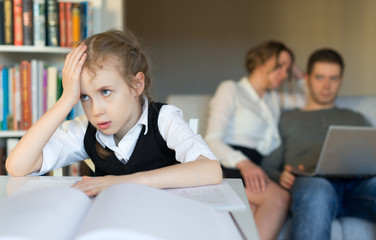 Fototapeta premium Tired little girl doing homework, while her parents resting on the sofa.