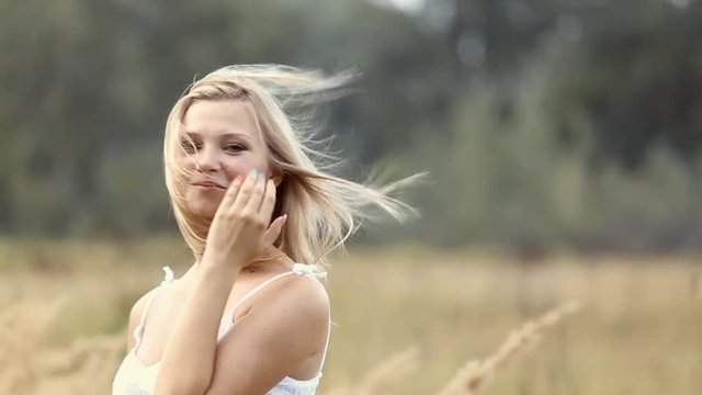 Beautiful young girl blowing kiss into camera smiling at blurry nature landscape background. Slow motion video footage.