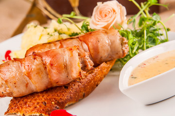 Meat patties wrapped in strips of bacon served with mashed potato