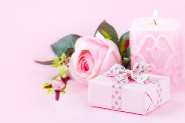 Fototapeta na wymiar Romantic setting with a wrapped gift, lit candle and a rose flower against pastel pink background. With copy space for your text