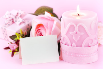 Beautiful festive setting - for Birthday, Engagement, St. Valentine's day occasion - with a greeting card, lit candle, roses and a gift against pastel pink background. With copy space for your text