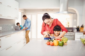 Woman teaching daughter to cut vegetables at table