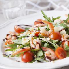 italian salad with shrimps, arugula, tomatoes, parmesan cheese, pine nut, olive oil and vinegar dressing on white plate. selective focus.