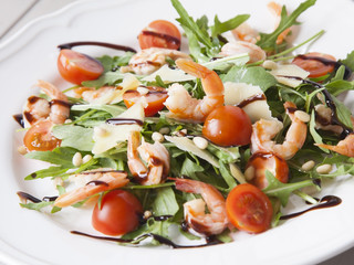 italian salad with shrimps, arugula, tomatoes, parmesan cheese, pine nut, olive oil and vinegar dressing on white plate. selective focus.