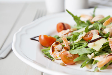 italian salad with shrimps, arugula, tomatoes, parmesan cheese, pine nut, olive oil and vinegar dressing on white plate. selective focus.