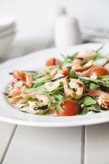 italian salad with shrimps, arugula, tomatoes, parmesan cheese, pine nut, olive oil and vinegar dressing on white plate. selective focus.