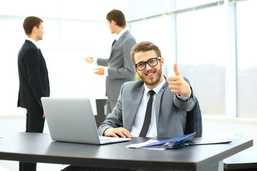 handsome young business man with people in background at office meeting. showing thumbs up