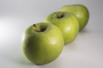 Three green apples aligned in a row on a white background