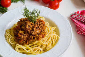 Spaghetti bolognese on white plate on white table.