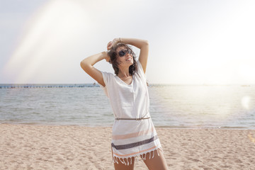 Woman in a tunic on the beach happy smiles and relaxes in the su - obrazy, fototapety, plakaty