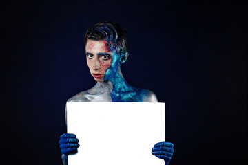 Crazy Screaming androgyne man with face art with POSTER. Blank for text. Aggressive. Freak person. Tinsel creative blue makeup. Intersex and anorexia concept. Space for logo. HOMOSEXUALITY