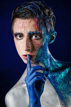 Crazy young androgyne man with face art. Freak person. Sperm on face. Tinsel creative blue makeup. Intersex and homosexuality concept. Space for logo
