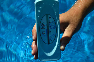 Woman holding hands in a water thermometer for pool during warm summer days. High temperature of waterpool 30 degrees Celsius in summertime