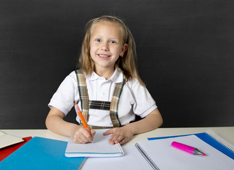 beautiful happy blond junior schoolgirl smiling while doing school homework writing on notepad with...
