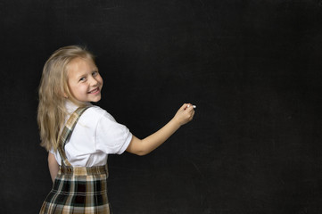 young sweet junior schoolgirl with blonde hair smiling happy writing with chalk in blackboard