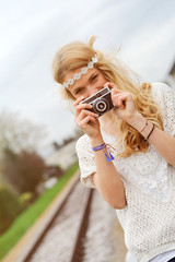 Junge Frau im Hippie-Look fotografiert am Bahnhof mit einer alten Analogkamera