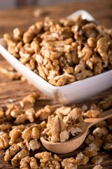 Heap of walnuts in font of white bowl on wooden spoon
