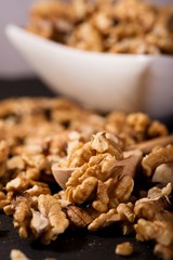 Walnuts spilled on black slate stone with bowl and spoon